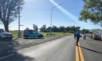 Agentes de seguridad vial y policía en una carretera de doble carril con líneas amarillas. Dos vehículos policiales estacionados a un lado bajo un cielo soleado