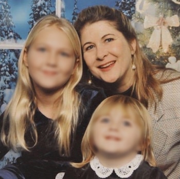 Una mujer sonriente posa junto a dos niñas de rostros difuminados frente a un fondo invernal y un árbol decorado