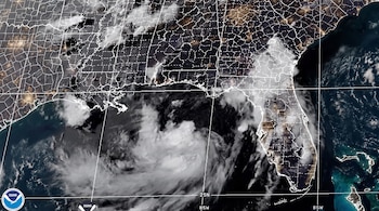 Imagen satelital de la costa del Golfo de México y el sureste de Estados Unidos con un gran sistema de nubes, luces de ciudades, fronteras y el logo de NOAA.