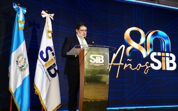 Un hombre con traje habla en un podio junto a la bandera de Guatemala y un panel conmemorativo del 80 aniversario de la Superintendencia de Bancos