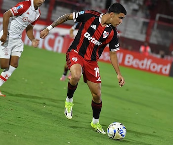 Un jugador de fútbol, Kendry Paez, con camiseta roja y negra, shorts rojos y medias negras, controla un balón en un campo de hierba verde