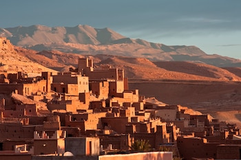 Edificaciones de adobe en ladera, montañas áridas de fondo, cielo despejado, iluminación cálida de atardecer
