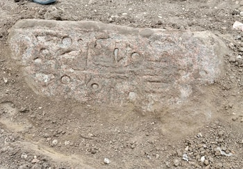 Un bloque de piedra tallado con grabados de jeroglíficos antiguos yace sobre la tierra y el polvo
