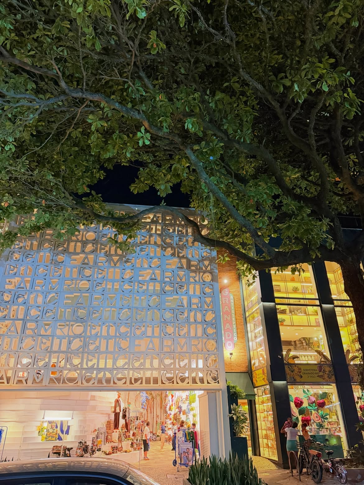 Una calle comercial de noche muestra las fachadas iluminadas de las tiendas Farm Rio