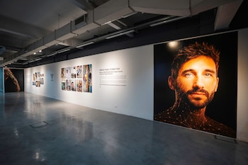Retrato a gran escala de un hombre junto a una pared blanca con varias fotografías de menor tamaño y un texto explicativo