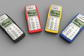 Cuatro teléfonos móviles Nokia 1100 en colores negro, rojo, amarillo y azul, alineados diagonalmente sobre una superficie gris