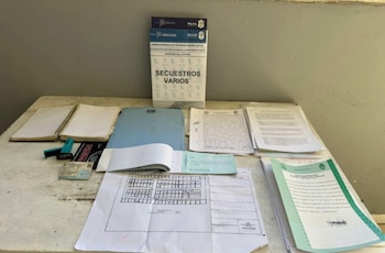 Una mesa con varios documentos apilados y esparcidos, un cuaderno abierto, una carpeta azul, y una pila de papeles con el título 'SECUESTROS VARIOS' de la Policía de Buenos Aires