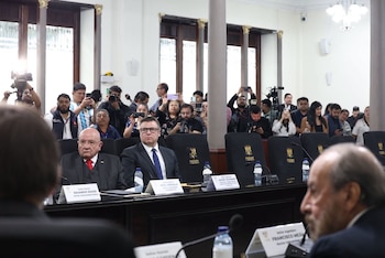 Tres hombres sentados en una mesa con placas de identificación: Eduardo Suger, Raúl Arévalo, Francisco Mejía. Detrás, una audiencia con teléfonos y cámaras