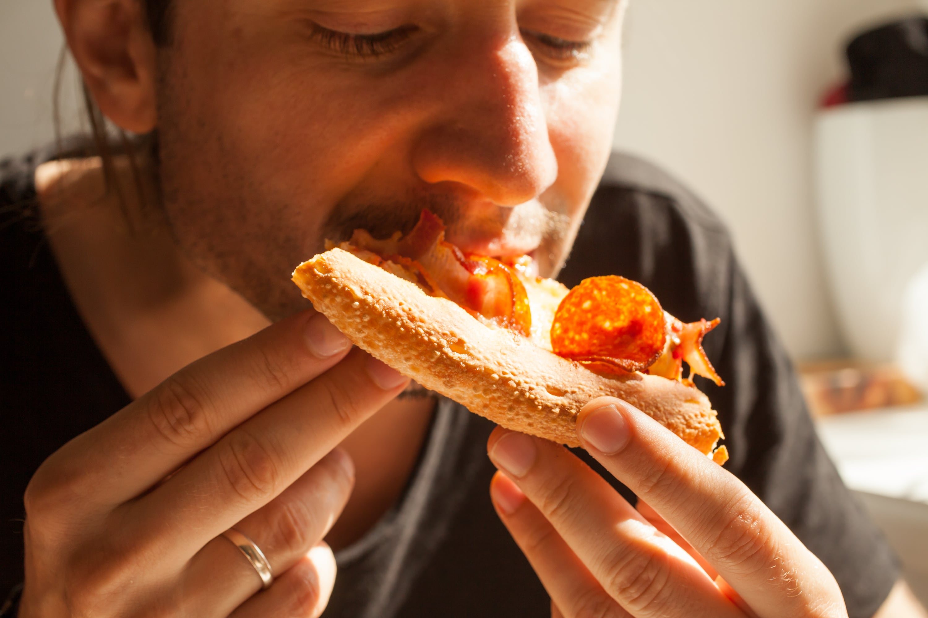 Un hombre comiendo una porción de pizza (AdobeStock)