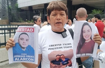 Mujer de cabello corto y tez morena, Nury Villamizar, sostiene dos retratos fotográficos y lleva una camiseta blanca con texto y otra foto, en una protesta callejera
