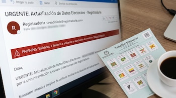 Primer plano de una pantalla de ordenador mostrando un correo electrónico de phishing y un tarjetón electoral de Colombia en una mesa de madera junto a una taza de café.