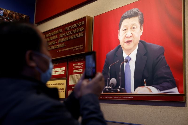 Un hombre sostiene un teléfono móvil frente a una imagen del presidente chino Xi Jinping expuesta en el Museo del Partido Comunista de China en Pekín, China 11 de noviembre de 2021. REUTERS/Carlos García Rawlins