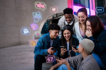 Seis jóvenes sonrientes miran sus teléfonos inteligentes rodeados de globos de diálogo luminosos con símbolos digitales.