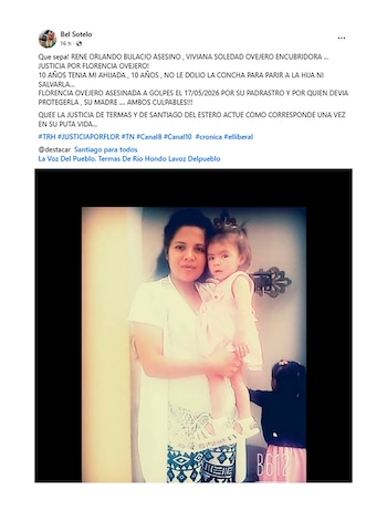 Una mujer de cabello oscuro sostiene a una niña pequeña con un vestido rosa. El rostro de la mujer mira directamente a la cámara. Otra niña se ve parcialmente a la derecha