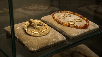 Joyas etruscas en vitrina: un broche de oro con figuras de animales y un collar de cuentas ámbar y oro con arracadas, exhibidos sobre cojines de terciopelo.
