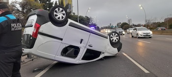 Vehículo utilitario blanco volcado sobre la calzada de una autopista. Un agente de la Policía de la Ciudad está de pie. Otros vehículos circulan
