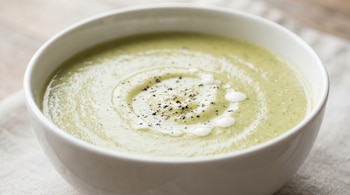 Primer plano de un plato sopero con sopa de crema de brócoli y manzana verde, tono verde pálido, con pimienta negra molida y gotas de crema.