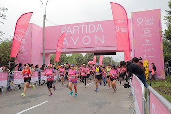 Varios corredores vestidos con camisetas deportivas cruzan el arco de salida rosa de una carrera en una calle flanqueada por vallas y banderas