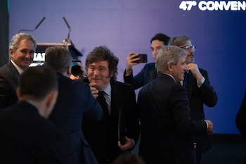 Javier Milei sonríe y saluda a un hombre de traje frente a un fondo azul con texto institucional