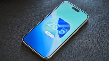 Teléfono inteligente con bordes claros sobre superficie de cuero negro. La pantalla muestra un ícono con "26.5 beta 3" en tonos azules y turquesa.