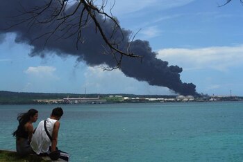 Una pareja se sienta cerca del mar mientras el humo se eleva sobre los tanques, el domingo (Reuters)