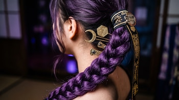 Vista posterior de una trenza morada sujeta con una cinta negra con bordados dorados y varias horquillas metálicas en el cabello.
