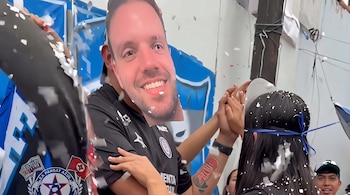 Varias personas celebran entre confeti blanco; una de ellas lleva una camiseta negra con la insignia de Cruz Azul y una máscara de cartón.