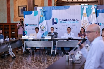 Funcionarios sentados en una mesa de reuniones con un banner de 'Planificación y Presupuesto Abierto 2027' y la bandera de Guatemala detrás