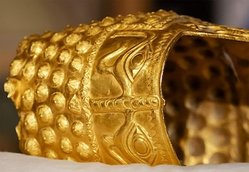 Primer plano de un casco antiguo de oro, el Casco de Coțofenești, con relieves de ojos y patrones geométricos, sobre una superficie clara