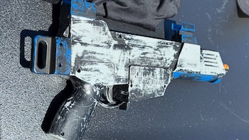 Pistola de juguete negra, blanca y azul con acabado desgastado. Se lee 'Waterbeast' en el costado. Descansa sobre una superficie oscura