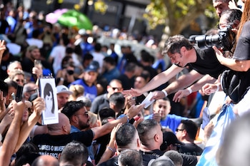 Axel Kicillof, vestido de negro, se inclina para saludar y estrechar manos a la multitud. La gente levanta teléfonos y carteles alrededor