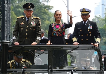 Claudia Sheinbaum sonríe y saluda con la mano desde un vehículo militar acompañada por dos mandos uniformados del Ejército y la Marina