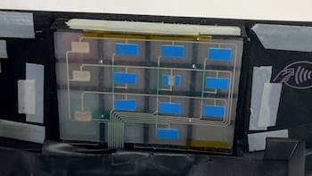 Componente electrónico transparente con cuadrícula de rectángulos azules y trazas. A la derecha, símbolo de pago sin contacto. Fijado con cinta adhesiva