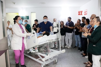 Un pasillo de hospital con personal médico aplaudiendo a un paciente en una cama. Una doctora empuja la cama mientras otros profesionales de la salud observan
