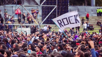 Una multitud de personas reunidas en un evento al aire libre donde una persona sostiene una bandera blanca con la palabra ROCK