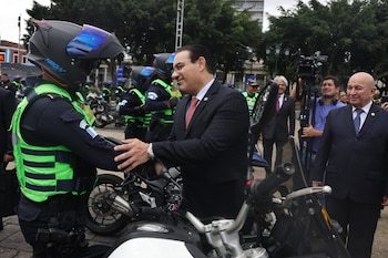 Un hombre en traje saluda a un policía con casco y chaleco reflectante junto a una fila de motocicletas