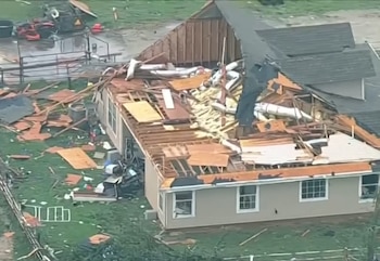 Vista aérea de una casa con el tejado parcialmente arrancado y escombros de madera dispersos en el césped tras el paso de un tornado