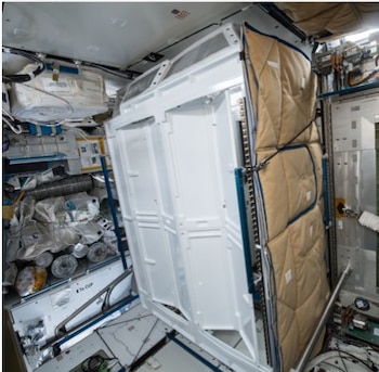 Estantes blancos de equipamiento, acolchado acolchado marrón y contenedores de almacenamiento en el interior de una estación espacial