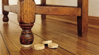 Pata de un mueble de madera apoyada sobre una rodaja de corcho junto a otras tres piezas redondas en un suelo de madera.