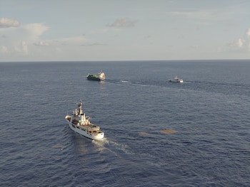 Vista aérea de un barco guardacostas blanco navegando en el océano cerca de un buque con contenedores y otras embarcaciones pequeñas