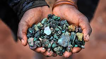Primer plano de dos manos con piel oscura sosteniendo un montón de pequeños trozos de minerales de colores verdes, negros y ocres