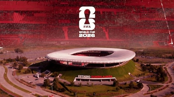 Vista aérea del Estadio Guadalajara con su techo blanco y gradas rojas, rodeado de áreas verdes y estacionamientos, y el logo del Mundial FIFA 2026 superpuesto.