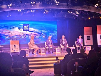 Cuatro panelistas, incluyendo exlíderes, sentados en un escenario iluminado con luces moradas frente a una pantalla grande que muestra la Tierra y el logo del WTTC, con una audiencia en la oscuridad