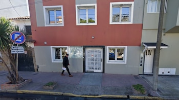 Edificio con fachada roja y gris, ventanas blancas, puerta blanca con "Residencia de Adultos Mayores David", hombre, acera, señal de tráfico, poste