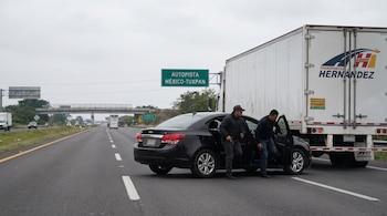 Dos hombres descienden de un automóvil negro que detiene un camión de carga blanco en la autopista México-Tuxpan. Un hombre porta una pistola.