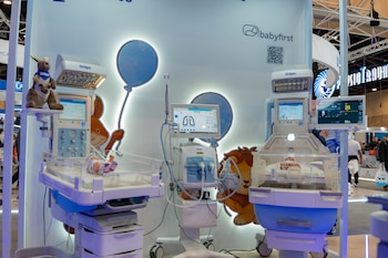 Dos incubadoras con monitores, un ventilador médico, un peluche de canguro, ilustraciones de un ratón y un león, logotipos Dräger y Babyfirst