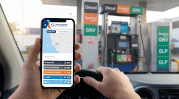 Una mano sostiene un teléfono móvil con una lista de precios frente al volante de un vehículo y los surtidores de una estación de servicio.