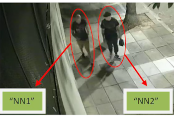 Una cámara de seguridad registra a dos hombres que entran por una puerta blanca hacia un garaje donde hay un vehículo estacionado