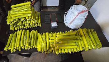 Pilas y filas de cartuchos amarillos, un rollo de cable blanco, una caja pequeña y tres teléfonos colocados sobre una mesa negra