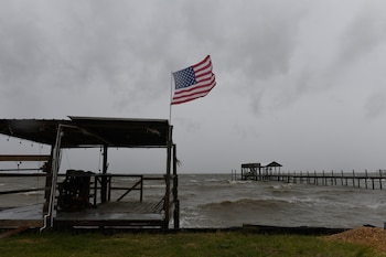 Una bandera de Estados Unidos ondea sobre un muelle de madera frente a un mar picado y un cielo nublado